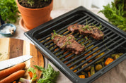 Svart ugnsform med galler och grillat kött samt grönsaker