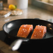 Svart non-stick stekpanna med två fiskbitar stekta i pannan