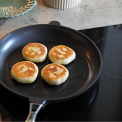 Svart stekpanna med non-stick yta, fyra stekta pannkakor i pannan