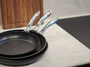 Set med keramiska non-stick stekpannor i mörkgrått, tre pannor med handtag i metall