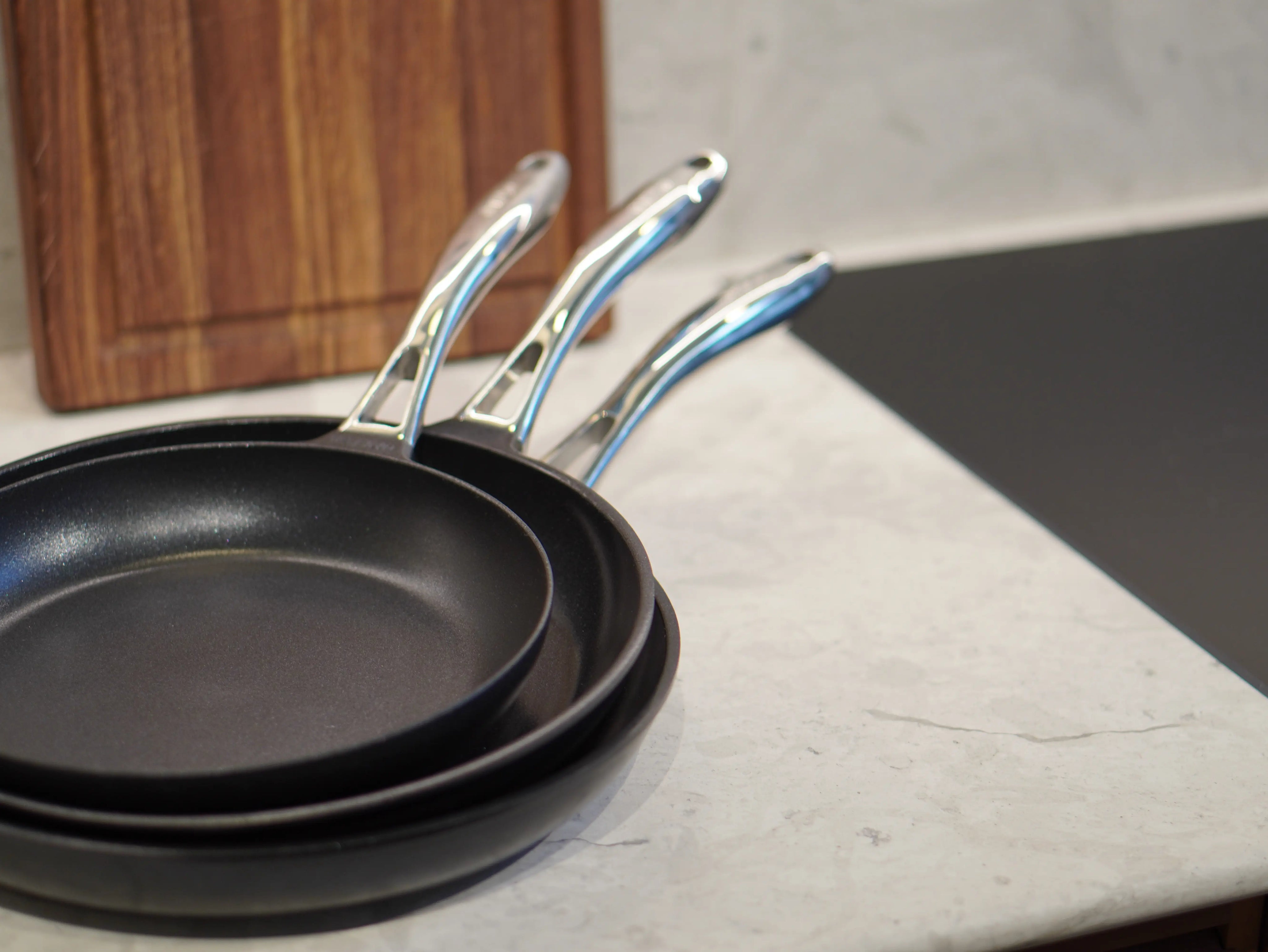 Set med keramiska non-stick stekpannor i mörkgrått, tre pannor med handtag i metall