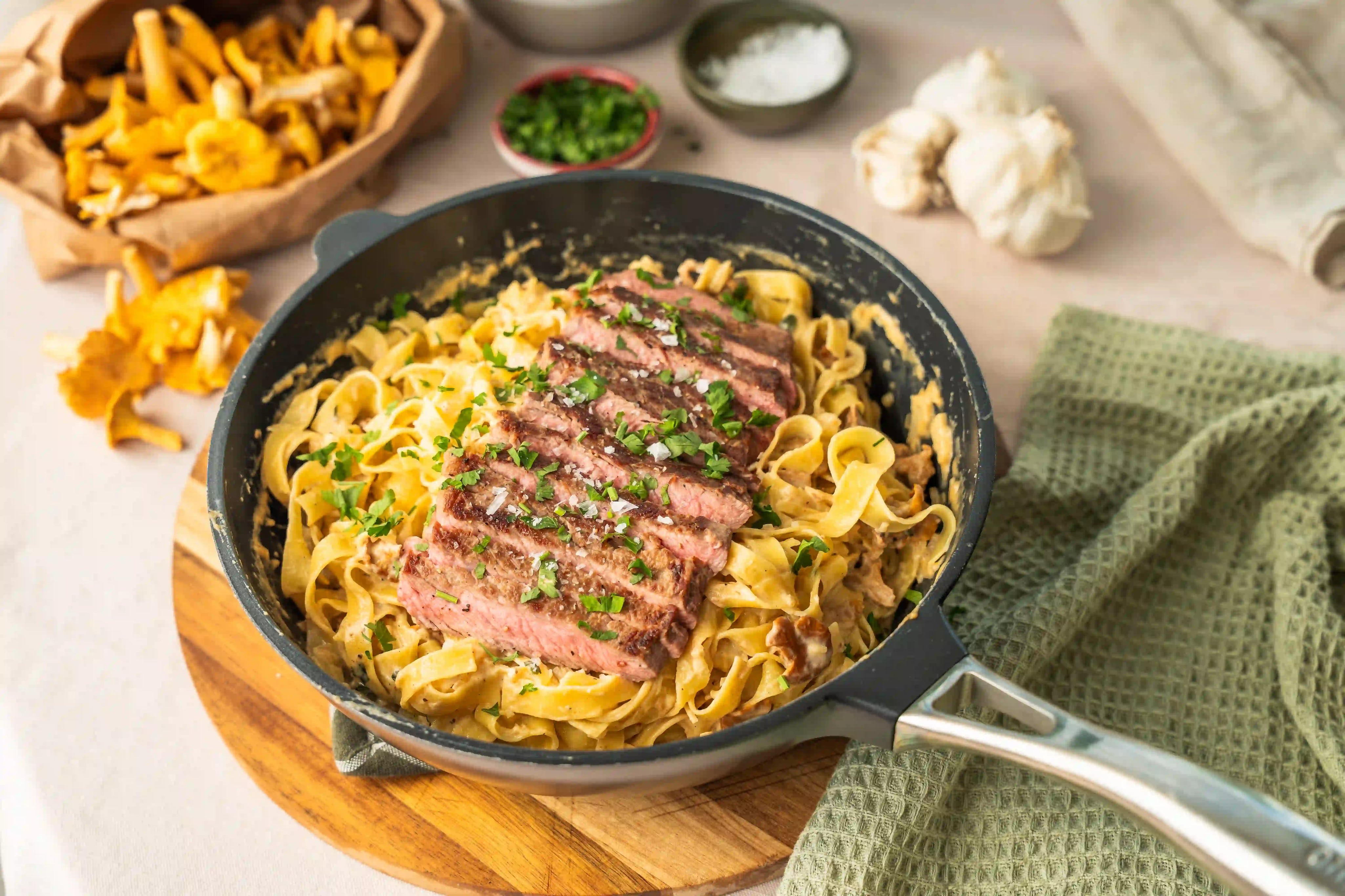 Djup stekpanna i svart med handtag, fylld med nudlar och kött.