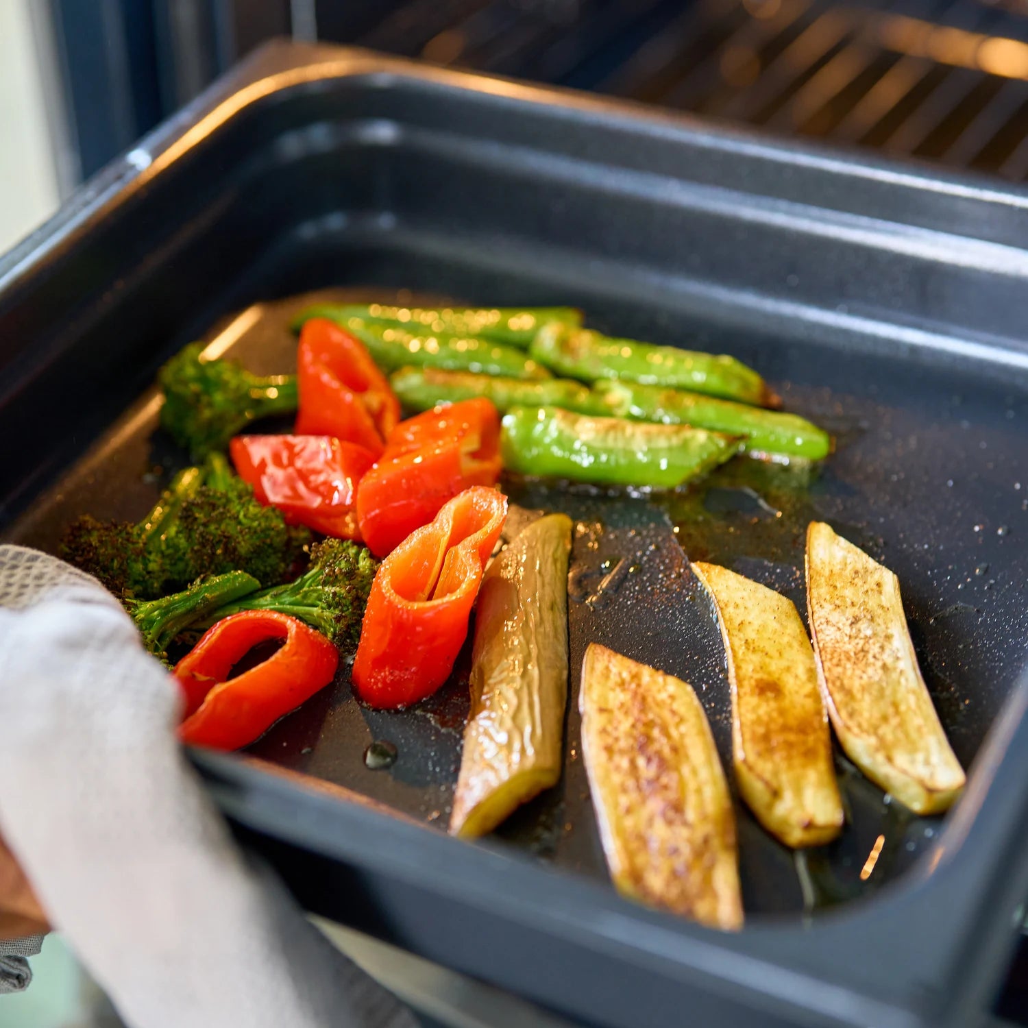 Ugnsform i mörkblått med non-stick, fylld med rostade grönsaker och tomater.