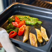 Ugnsform i mörkblått med non-stick, fylld med rostade grönsaker och tomater.