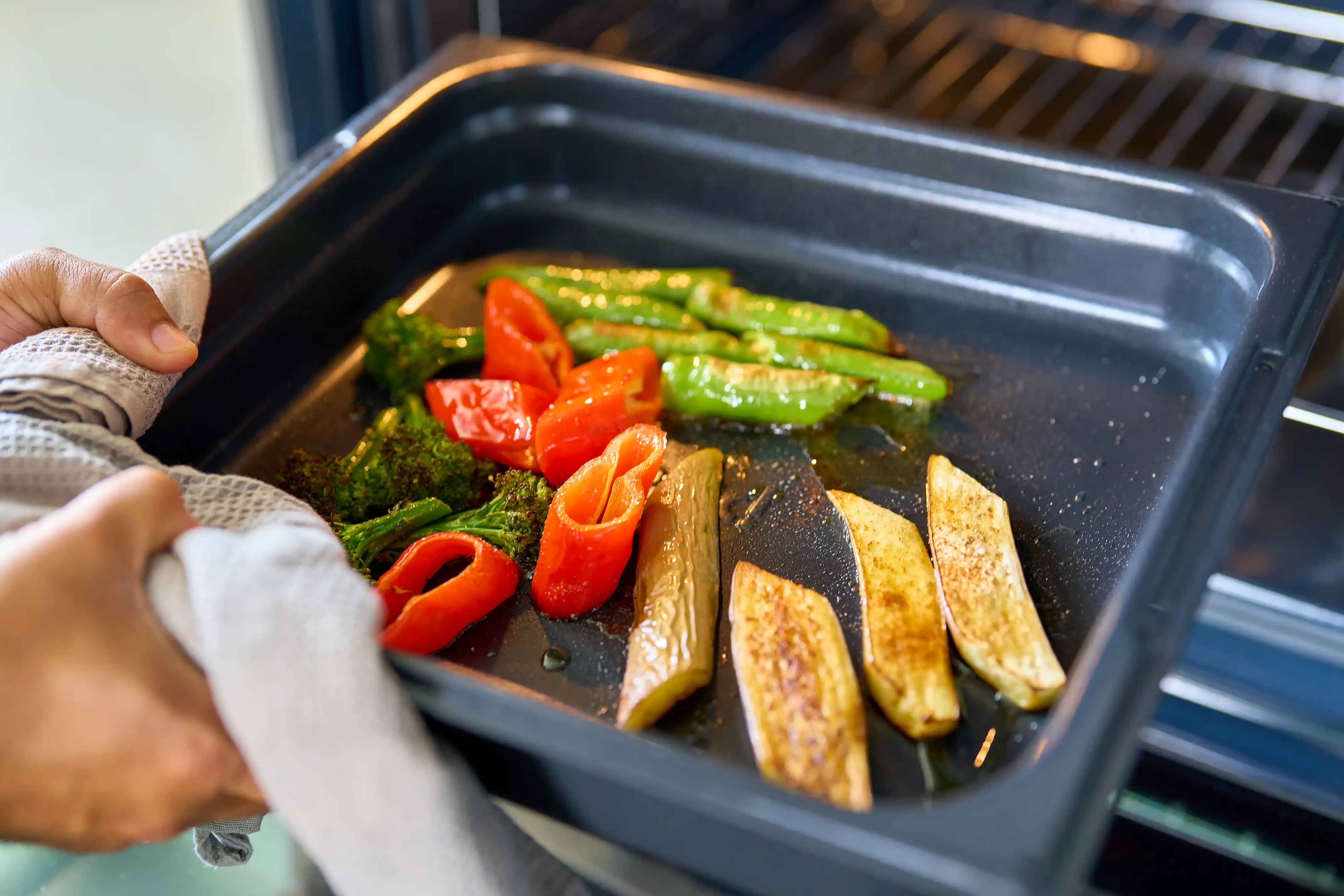 Svart ugnsform med galler, fylld med grillade grönsaker