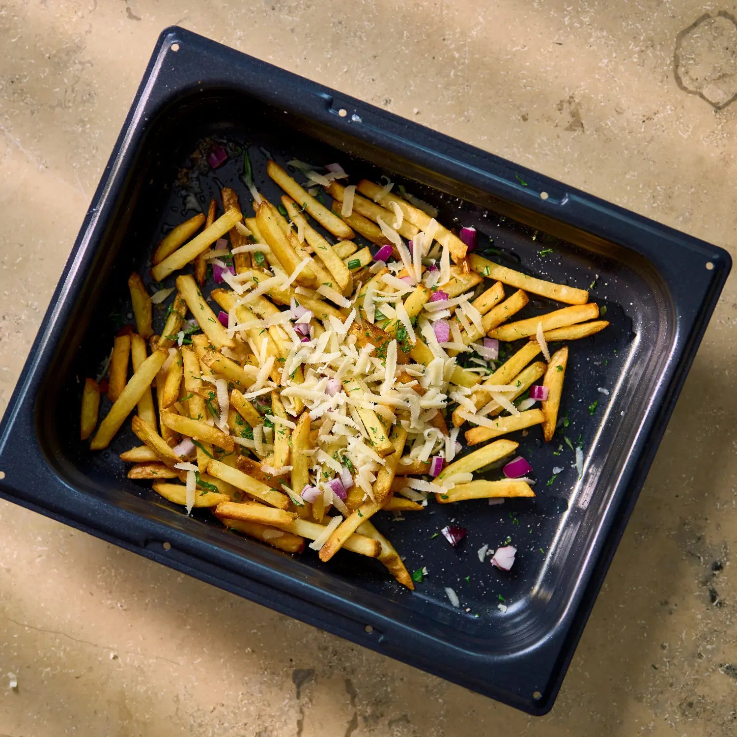 Ugnsform i mörkblått med non-stick, fylld med rostade grönsaker och strössel.