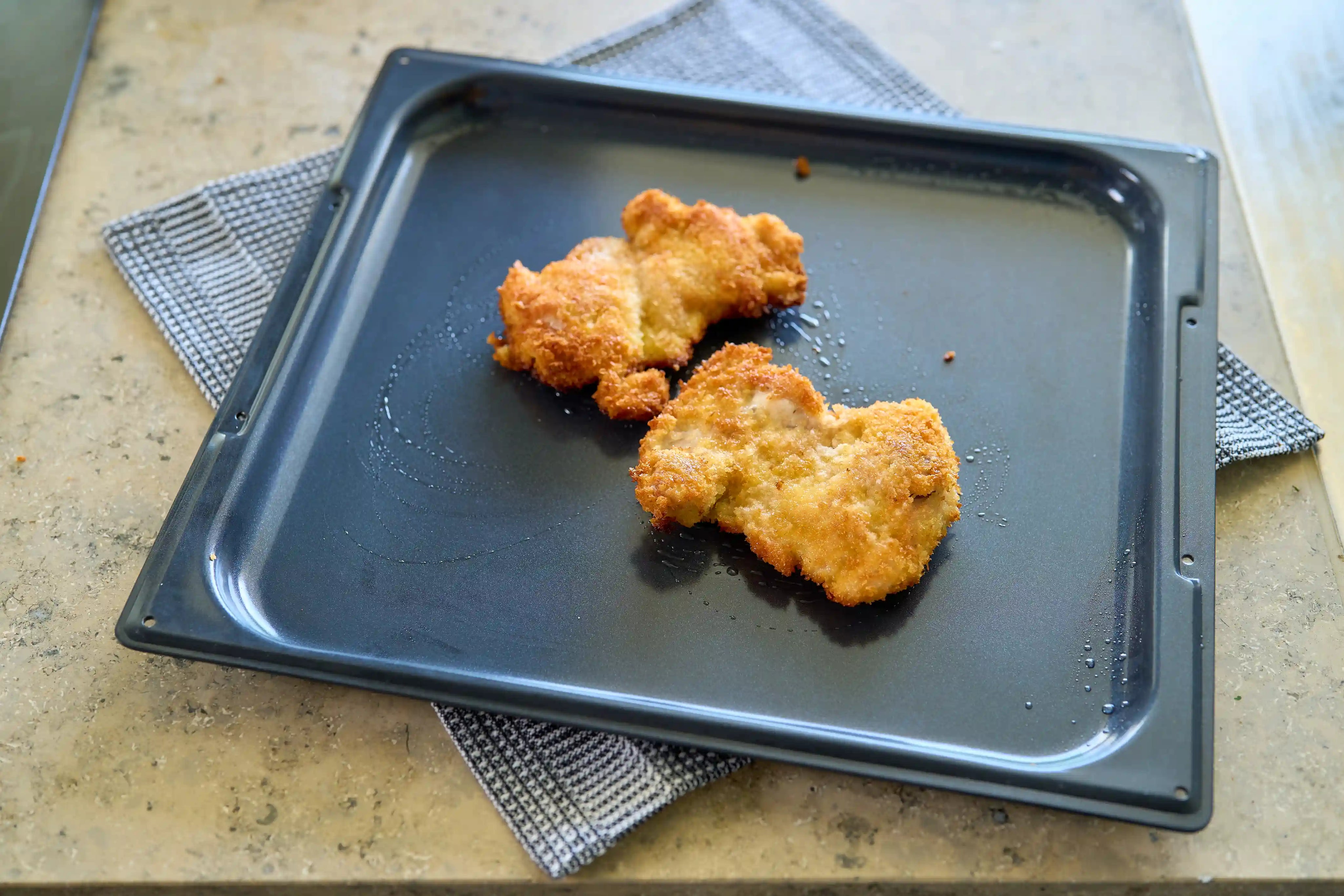 Pizzaplåt i non-stick med stekta kycklingbitar på ugnsplåt.