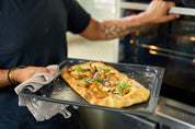 Pizzaplåt i non-stick med pizza i ugnen, plåten håller av person.
