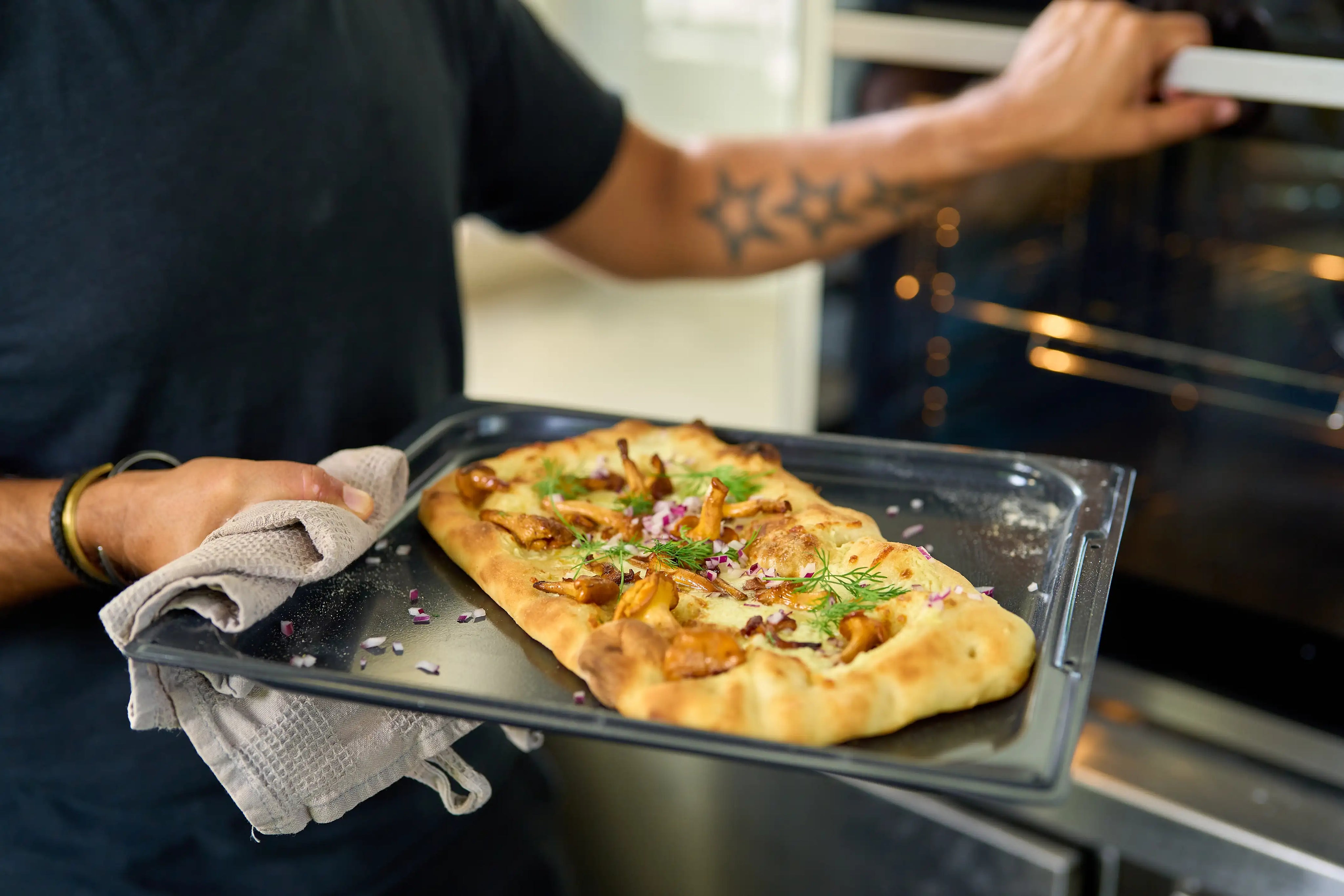 Pizzaplåt i non-stick med pizza i ugnen, plåten håller av person.